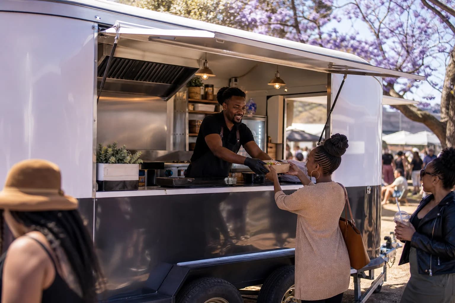 A vendor serving a customer from the lit serving hatch of a mobile food trailer
